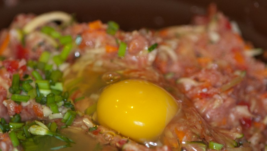 raw egg sitting on top of raw minced meat with chives