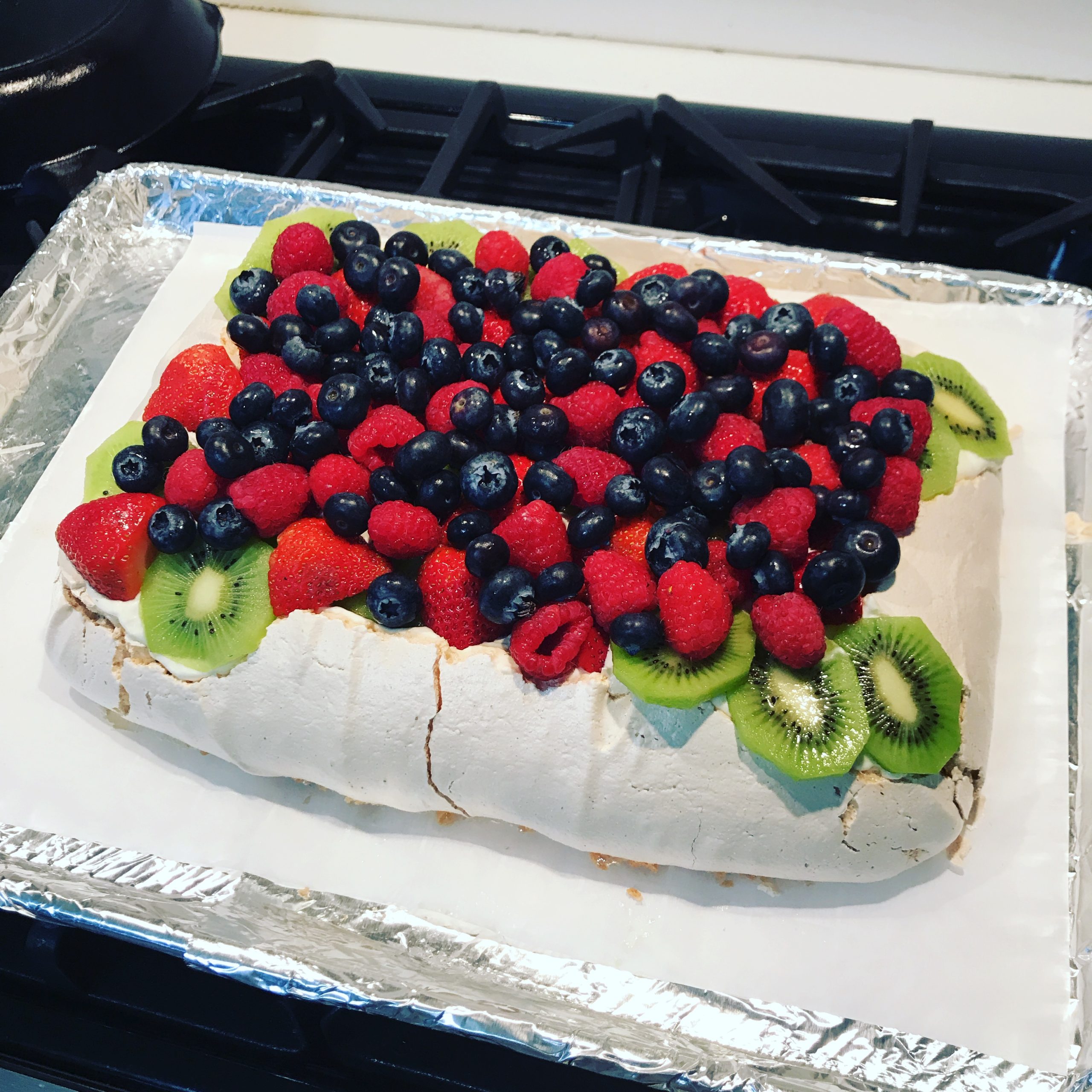 Pavalova covered in Raspberries and blueberries with kiwi on the side